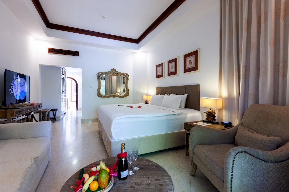 Hotelzimmer mit einem Bett, einer Lampe, einem Tisch mit Flasche und Gläsern, und Dekoration.