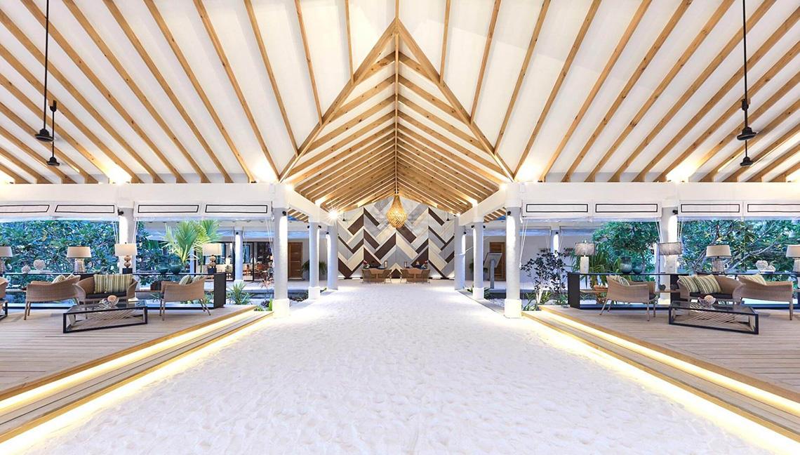 Hotellobby des Amari Havodda Maldives mit weißem Sandboden und Holzdecken.