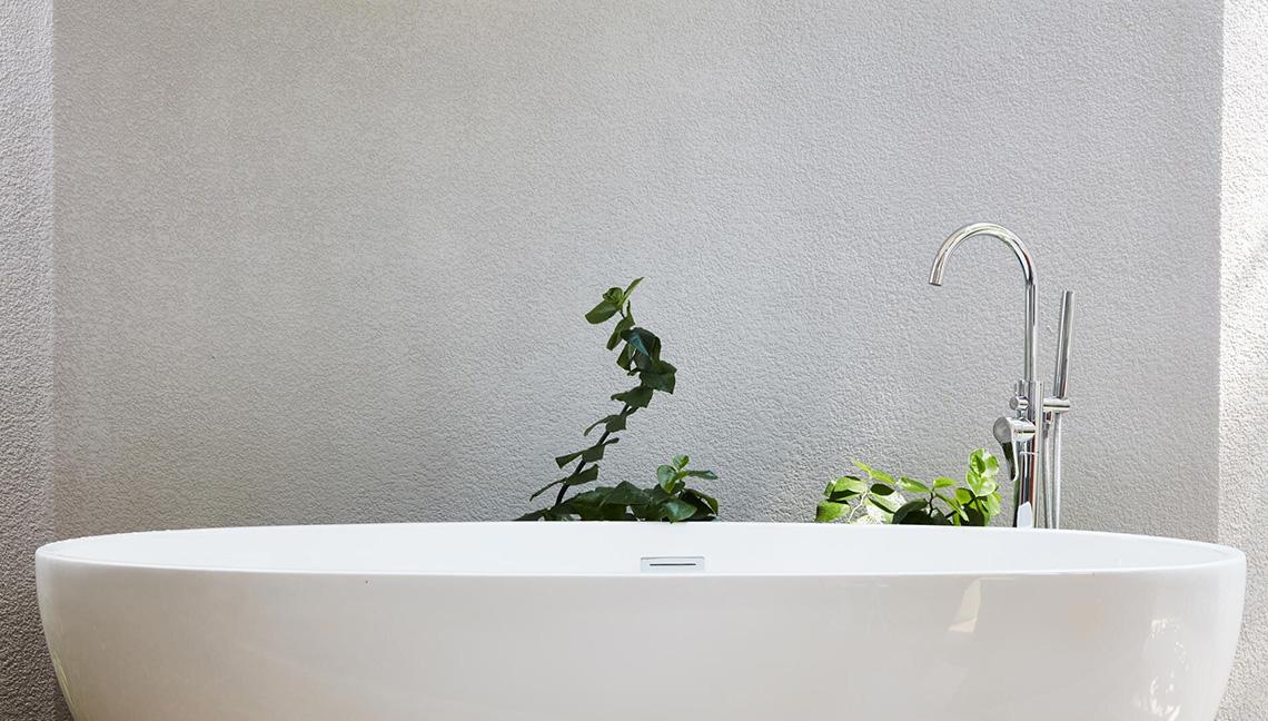 Weiße Badewanne im Badezimmer des Amari Havodda Hotels mit einem Hahn und Pflanzen im Hintergrund.