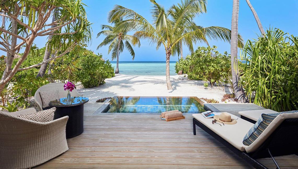 Außenbereich des Amari Havodda Maldives mit Pool, Strand und Palmen.