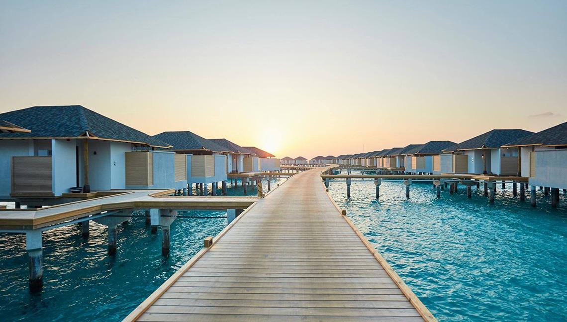 Sonnenuntergang am Amari Havodda Maldives mit Wasservillen auf Stegen im Wasser.