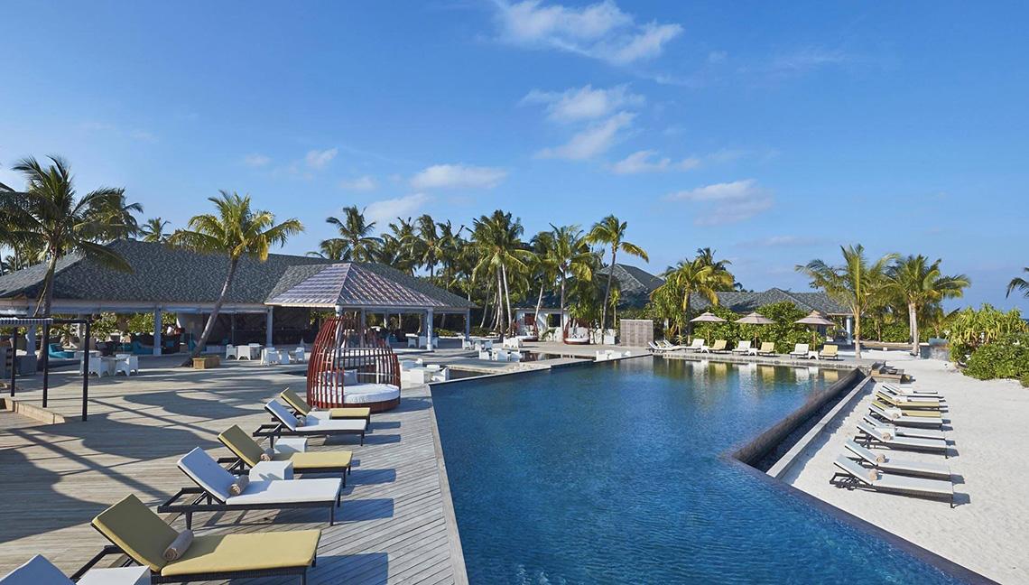 Außenpoolbereich des Amari Havodda Maldives Hotels mit vielen Liegestühlen und Palmen.