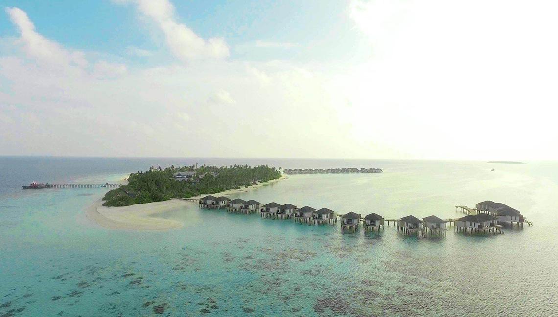 Aerial view of Amari Havodda Maldives resort with water bungalows and a pier
