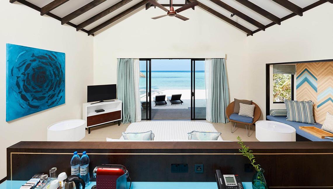 Innenansicht eines Zimmers im Amari Havodda Maldives mit einem Bett, Fernseher, und Meerblick.