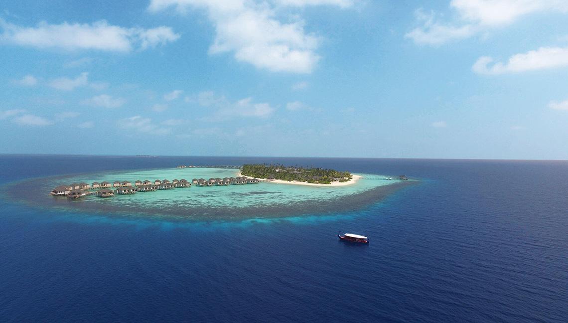 Aerial view of Amari Havodda Maldives with bungalows on a small island surrounded by blue water.