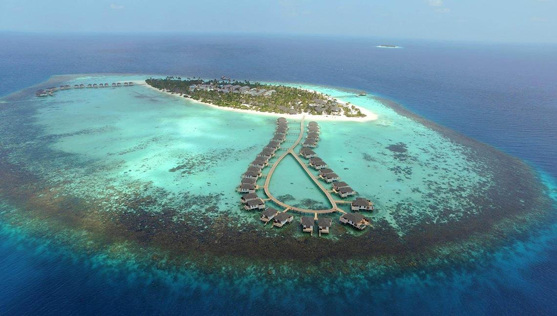 Luftaufnahme des Amari Havodda Maldives Resorts auf einer Insel mit türkisfarbenem Wasser und Riffen