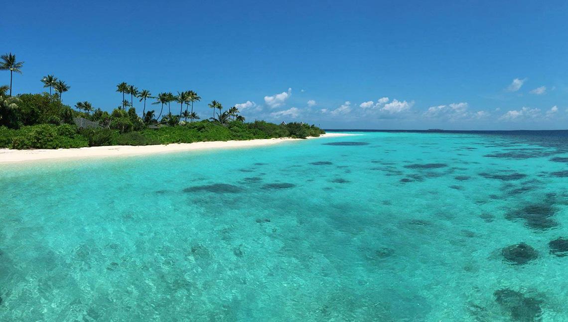 Strand des Amari Havodda Hotels auf den Malediven mit kristallklarem Wasser und weißem Sand.