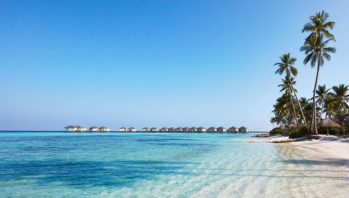Strand des Amari Havodda Maldives mit Wasservillen und Palmen