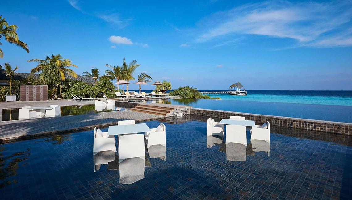 Außenpoolbereich des Amari Havodda Maldives mit weißen Tischen und Stühlen.