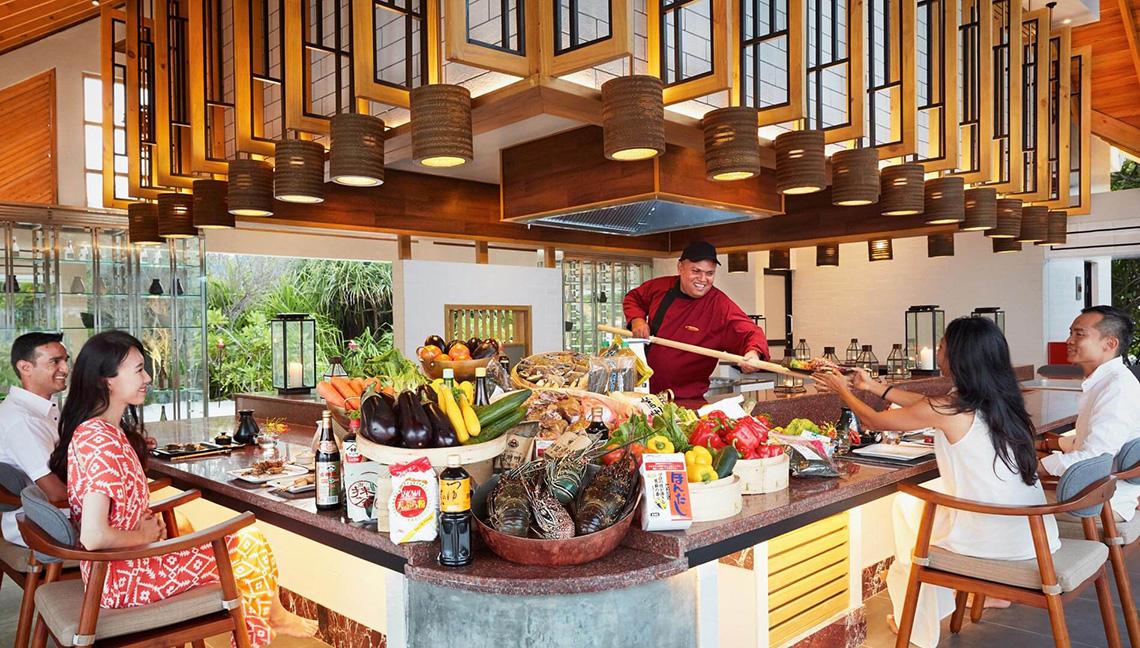 Menschen sitzen an einem Buffettisch im Amari Havodda Maldives Hotel und essen mit einem Koch.