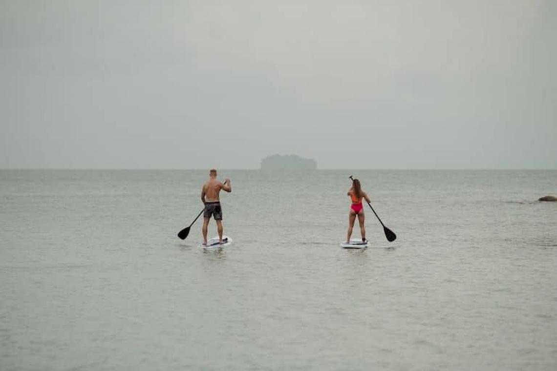 Zwei Paddler im Meer, einer in Badehose und die andere in Bikini, beide auf Paddelbrettern.