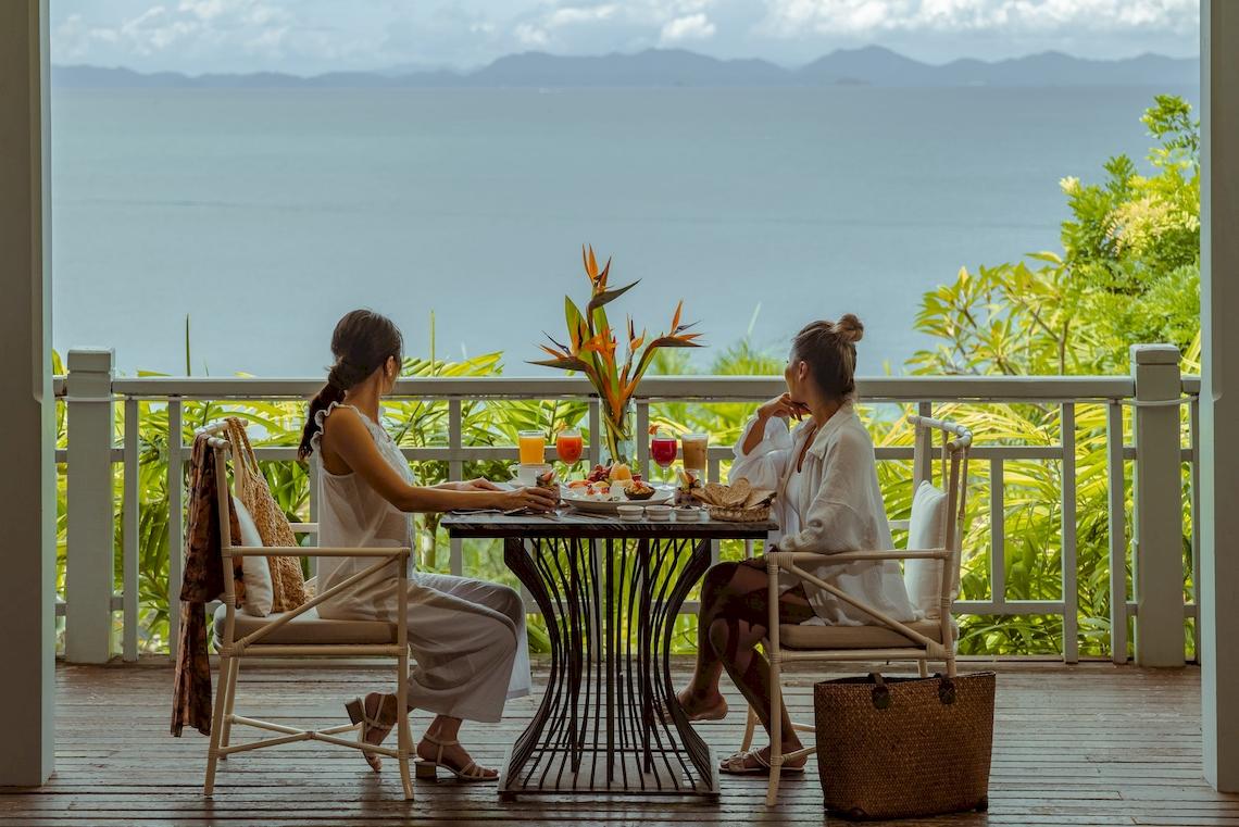 Zwei Frauen frühstücken auf der Balkonterrasse des Amatara Welleisure Resorts mit Meerblick.