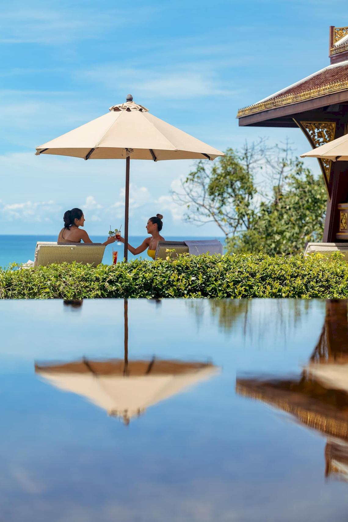Zwei Frauen am Pool des Amatara Welleisure Resort, die Getränke genießen.