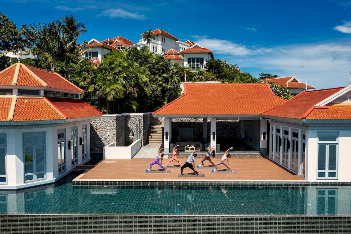 Gruppe von Menschen, die Yoga vor dem Amatara Welleisure Resort am Pool praktizieren.