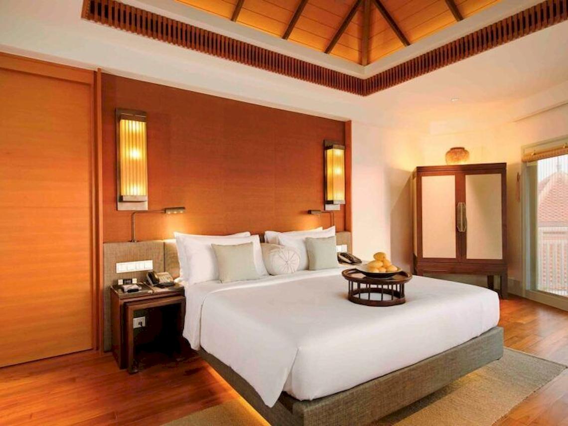 Hotelzimmer im Amatara Welleisure Resort mit großem Bett, Tisch mit Früchten und Holzmöbeln.