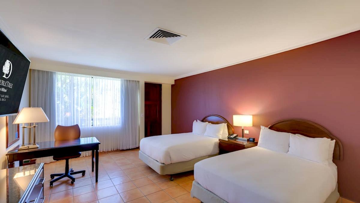 Doppelzimmer im DoubleTree by Hilton Hotel Cariari San Jose mit zwei Betten, Schreibtisch und Fenstern.