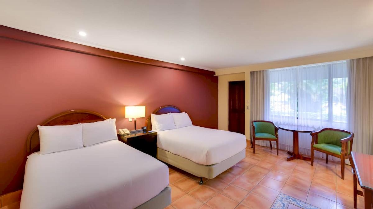 Doppelzimmer im DoubleTree by Hilton Hotel Cariari San Jose mit zwei Betten, Tisch, Stühlen und Fenstern.