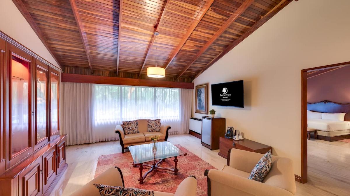 Wohnzimmer im DoubleTree by Hilton Hotel Cariari San Jose mit beigem Sofa, Glastisch und Fernseher.