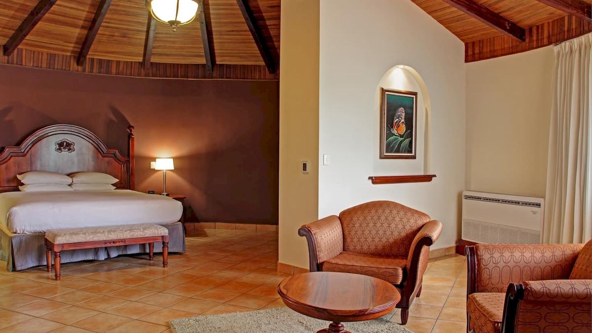 Doppelzimmer im DoubleTree by Hilton Hotel Cariari San Jose mit Bett, Nachttisch, Lampe, Teppich und zwei Sesseln.