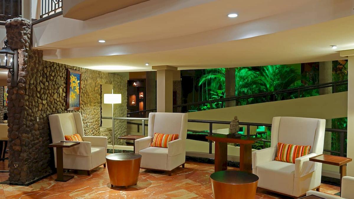 Lobby des DoubleTree by Hilton Hotel Cariari San Jose mit weißen Sesseln, Tischen und einer Steinwand.