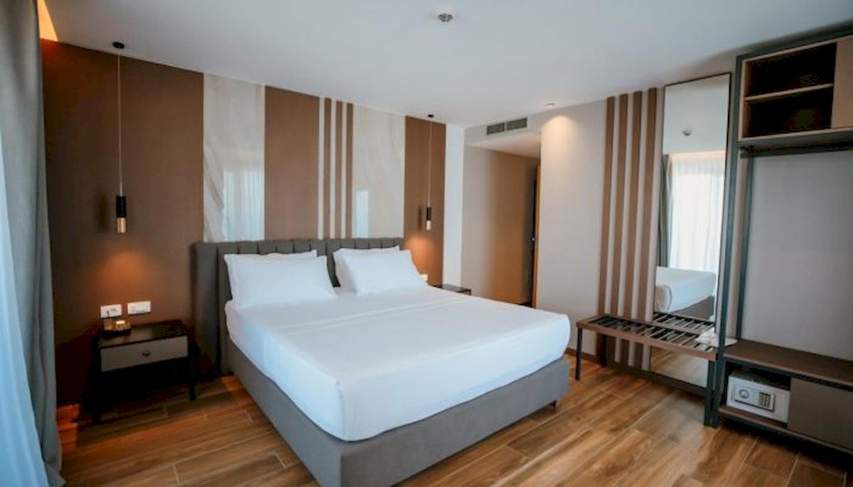 Schlafzimmer im Klajdi Resort & SPA Hotel mit einem großen Bett und weißen Laken, zwei Nachttischen und einem Spiegel.
