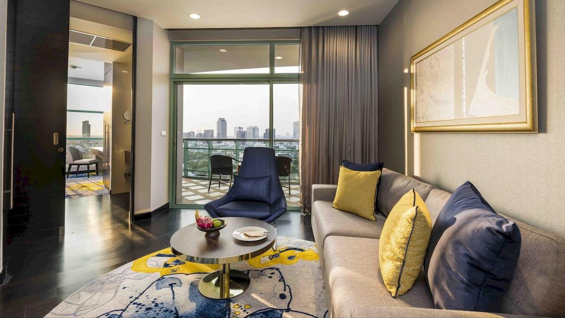 Das Wohnzimmer im Chatrium Hotel Riverside Bangkok mit einem Sofa, einem Tisch und einem Balkon mit Stadtblick.