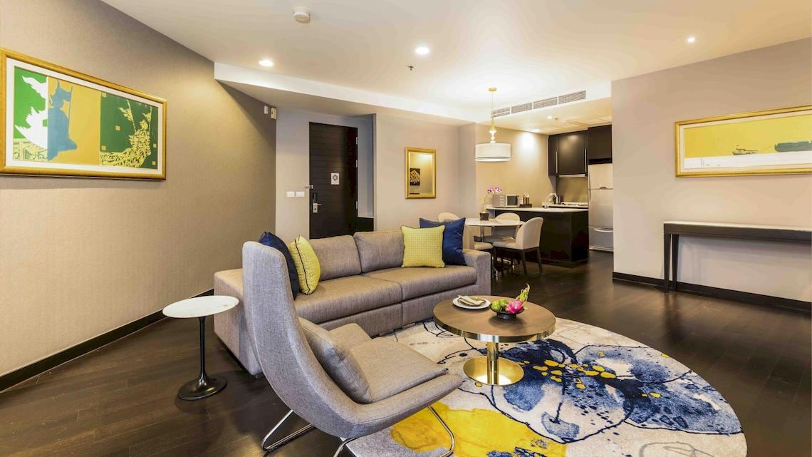 Wohnzimmer des Chatrium Hotel Riverside Bangkok mit Sofa, Tisch und Esstisch.