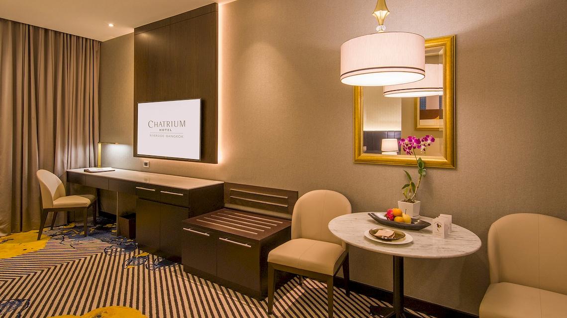 Innenansicht eines Zimmers im Chatrium Hotel Riverside Bangkok mit Schreibtisch, Stühlen und Tisch.