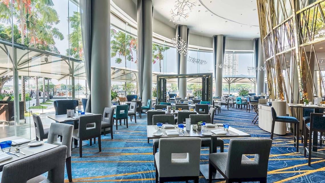 Innenansicht des Restaurants im Chatrium Hotel Riverside Bangkok mit blauen Teppichboden und modernen Möbeln.