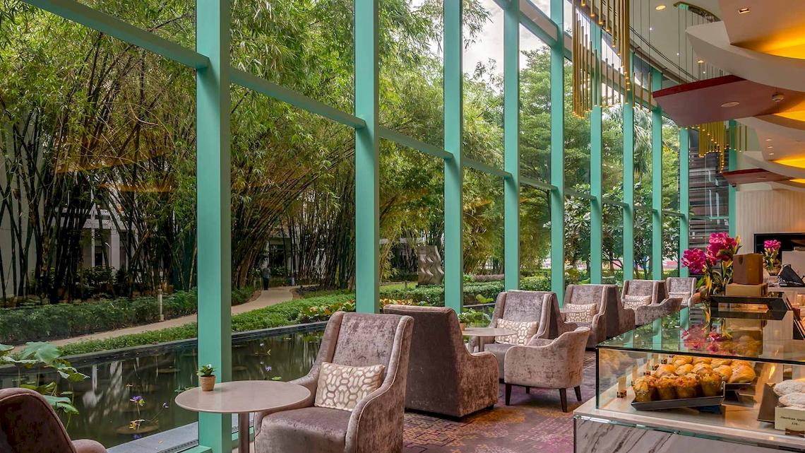 Lounge-Bereich im Chatrium Hotel Riverside Bangkok mit großen Fenstern und Blick auf den Garten.