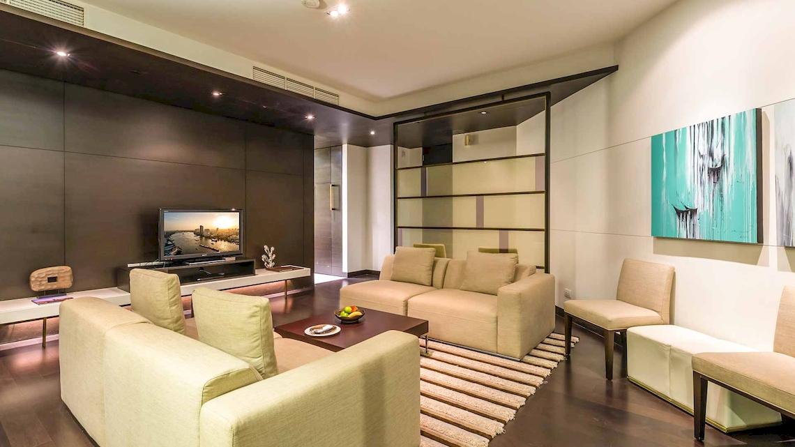 Wohnzimmer im Chatrium Hotel Riverside Bangkok mit Fernseher, Sofas und Kunstwerken an der Wand.