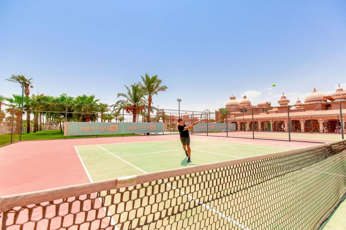Tennisplatz im Pickalbatros Aqua Vista Resort Hotel mit einem Spieler, der einen Ball schlägt.