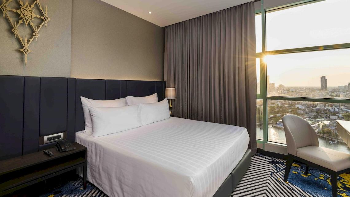 Hotelzimmer im Chatrium Hotel Riverside Bangkok mit Bett, Schreibtisch und Flussblick.