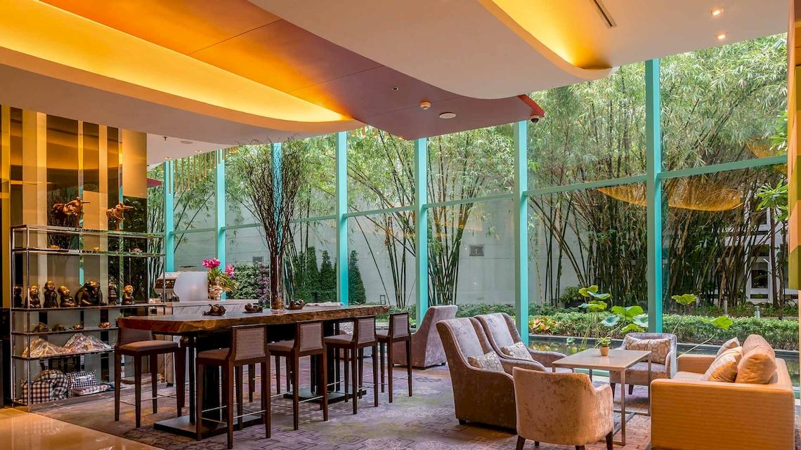 Lobby des Chatrium Hotel Riverside Bangkok mit großen Fenstern und Blick auf Bäume.