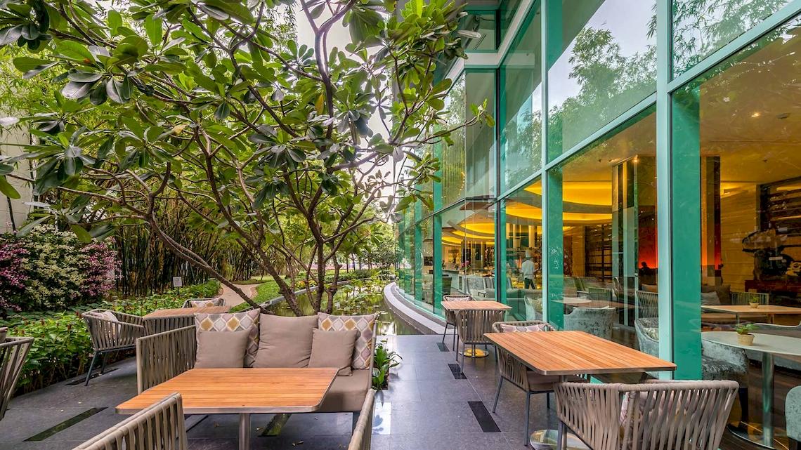 Außenterrasse des Chatrium Hotel Riverside Bangkok mit Tischen, Stühlen und Pflanzen.