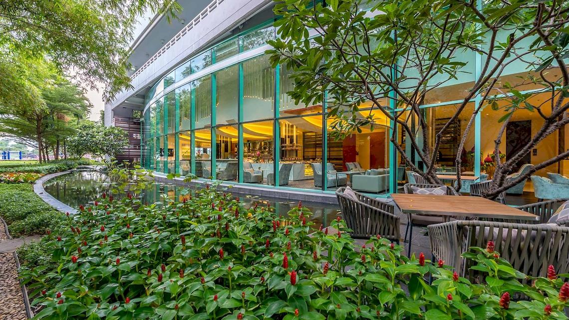 Außenbereich des Chatrium Hotel Riverside Bangkok mit Außensitzen und grünen Pflanzen.