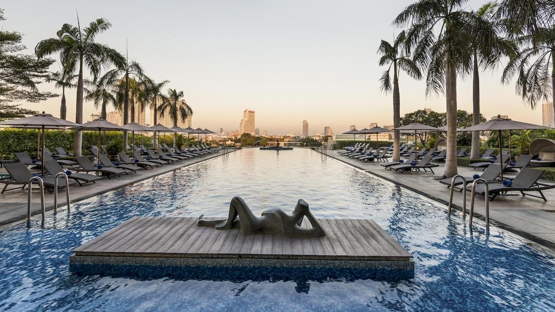 Ein großer Swimmingpool mit Sonnenliegen und Sonnenschirmen im Chatrium Hotel Riverside Bangkok