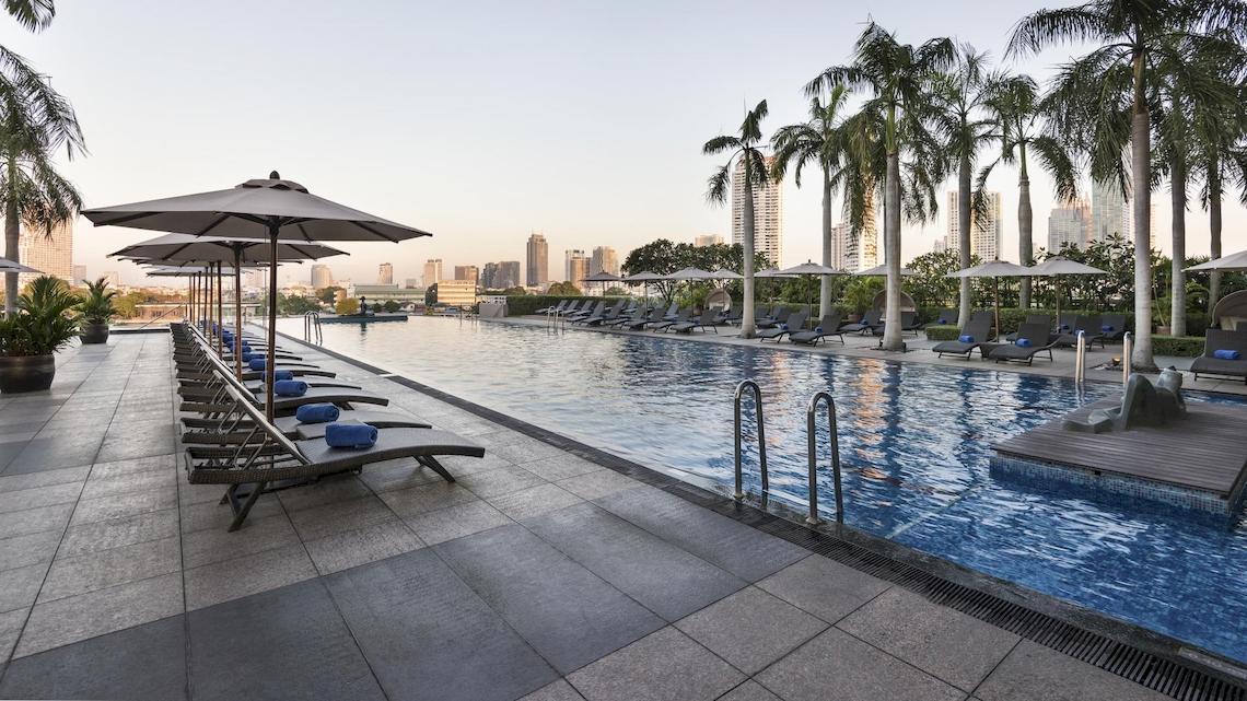 Loungebereich mit Sonnenliegen und Schirmen am Pool des Chatrium Hotel Riverside Bangkok.