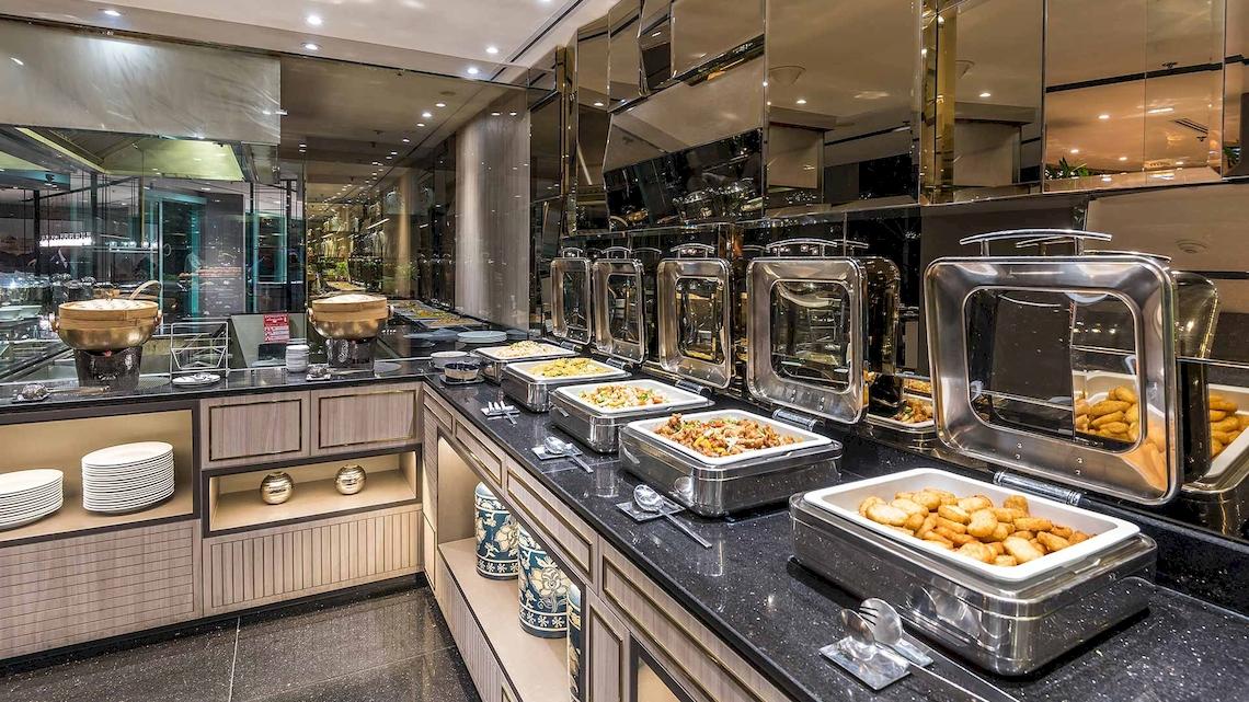 Speisenbereich im Chatrium Hotel Riverside Bangkok mit Edelstahlbuffets und Tellern.