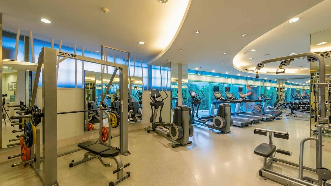Fitnesscenter im Chatrium Hotel Riverside Bangkok mit modernen Geräten und großen Fenstern.