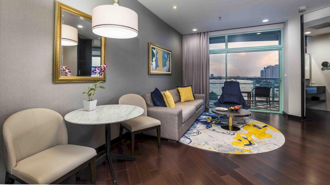 Wohnzimmer des Chatrium Hotel Riverside Bangkok mit Couch, Tischen und Aussicht auf die Stadt.