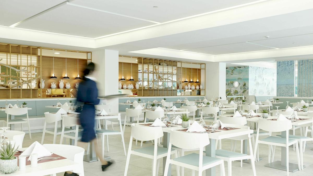 Innenansicht des Restaurants im Iberostar Cristina Hotel mit modernen weißen Tischen und Stühlen.