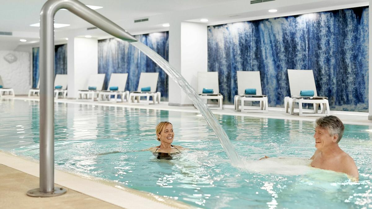 Ein Schwimmbad im Iberostar Cristina Hotel mit Wasserfall und zwei Personen, die darin schwimmen.