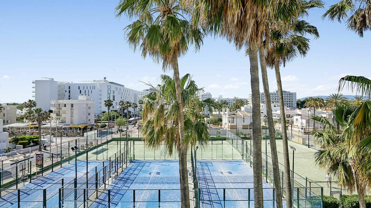 Aussicht auf Tennisplatz im Hotel Iberostar Cristina mit mehreren Palmen und Gebäuden im Hintergrund.