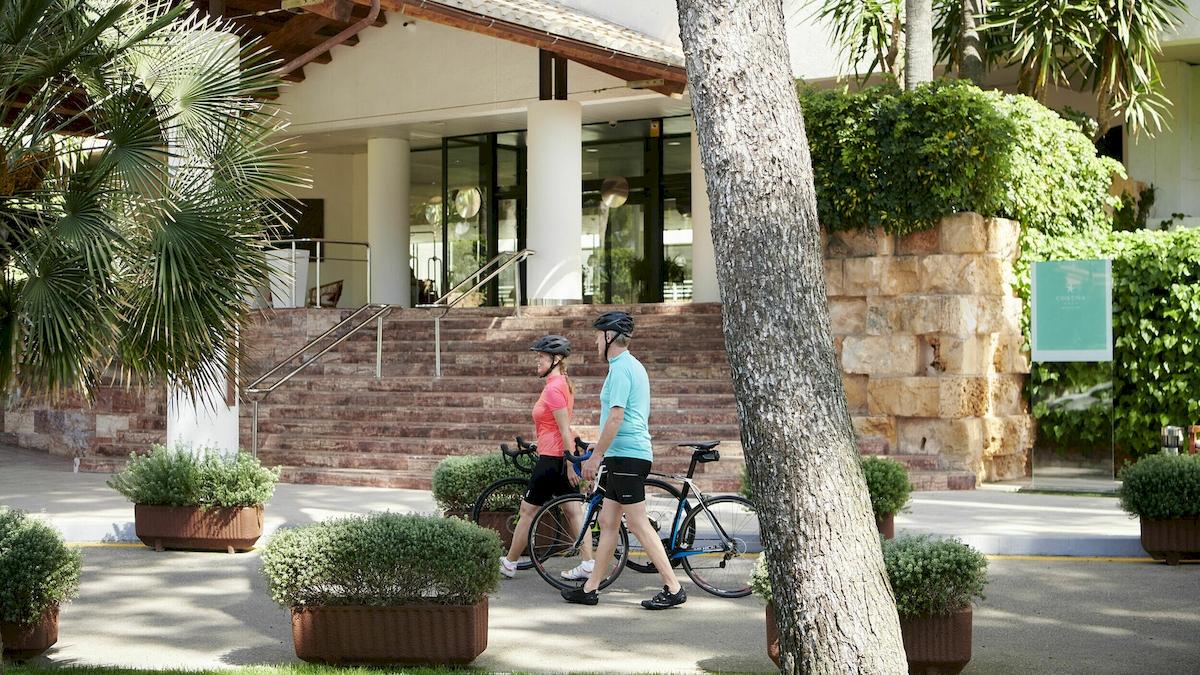 Zwei Leute mit Fahrrad vor dem Iberostar Cristina Hotel im Freien