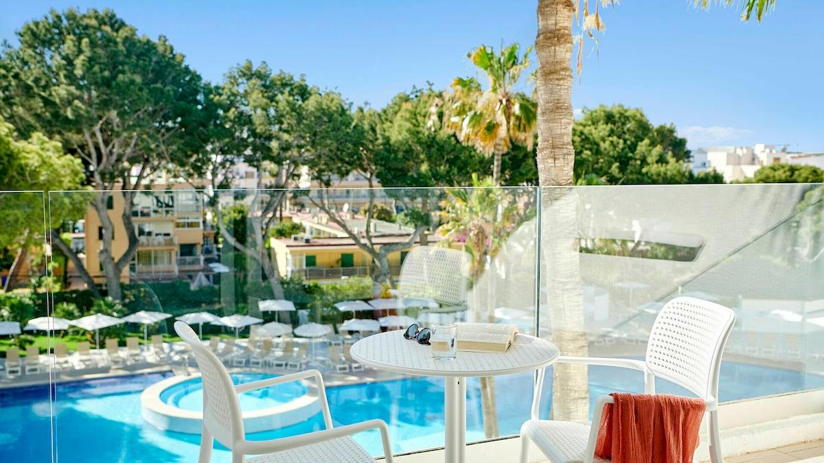 Balkon des Iberostar Cristina Hotels mit Aussicht auf den Swimmingpool, umgeben von Bäumen und Sonnenschirmen.