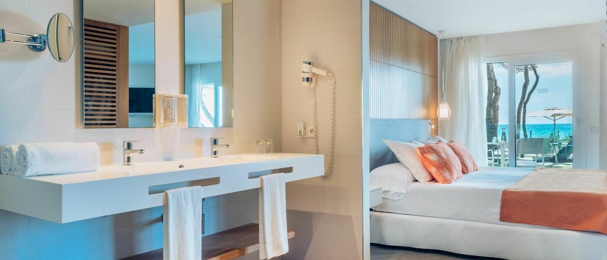Innenansicht eines Hotelzimmers im Iberostar Playa de Muro, mit Blick auf ein modernes Badezimmer und ein gemütliches Bett.