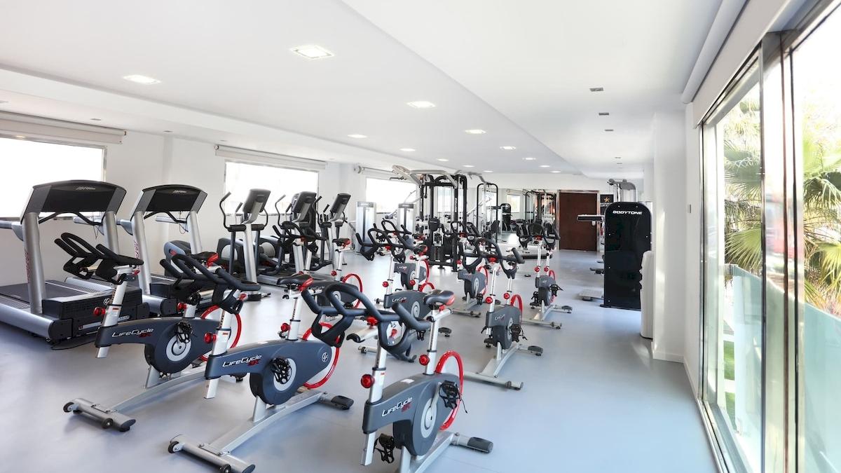Fitnessraum im Iberostar Playa de Muro mit verschiedenen Trainingsgeräten wie Laufbändern und Spinrädern.
