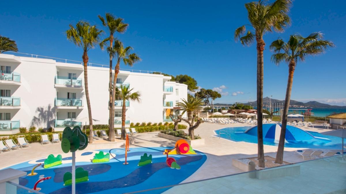 Außenbereich des Iberostar Playa de Muro Hotels mit Swimmingpool, Spielplatz und Sonnenliegen.