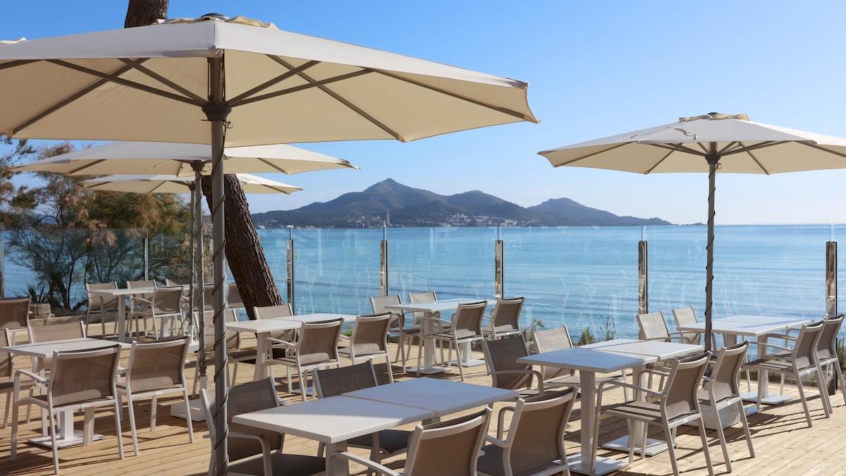 Terrasse des Iberostar Playa de Muro Hotels mit Tischen und Sonnenschirmen am Meer